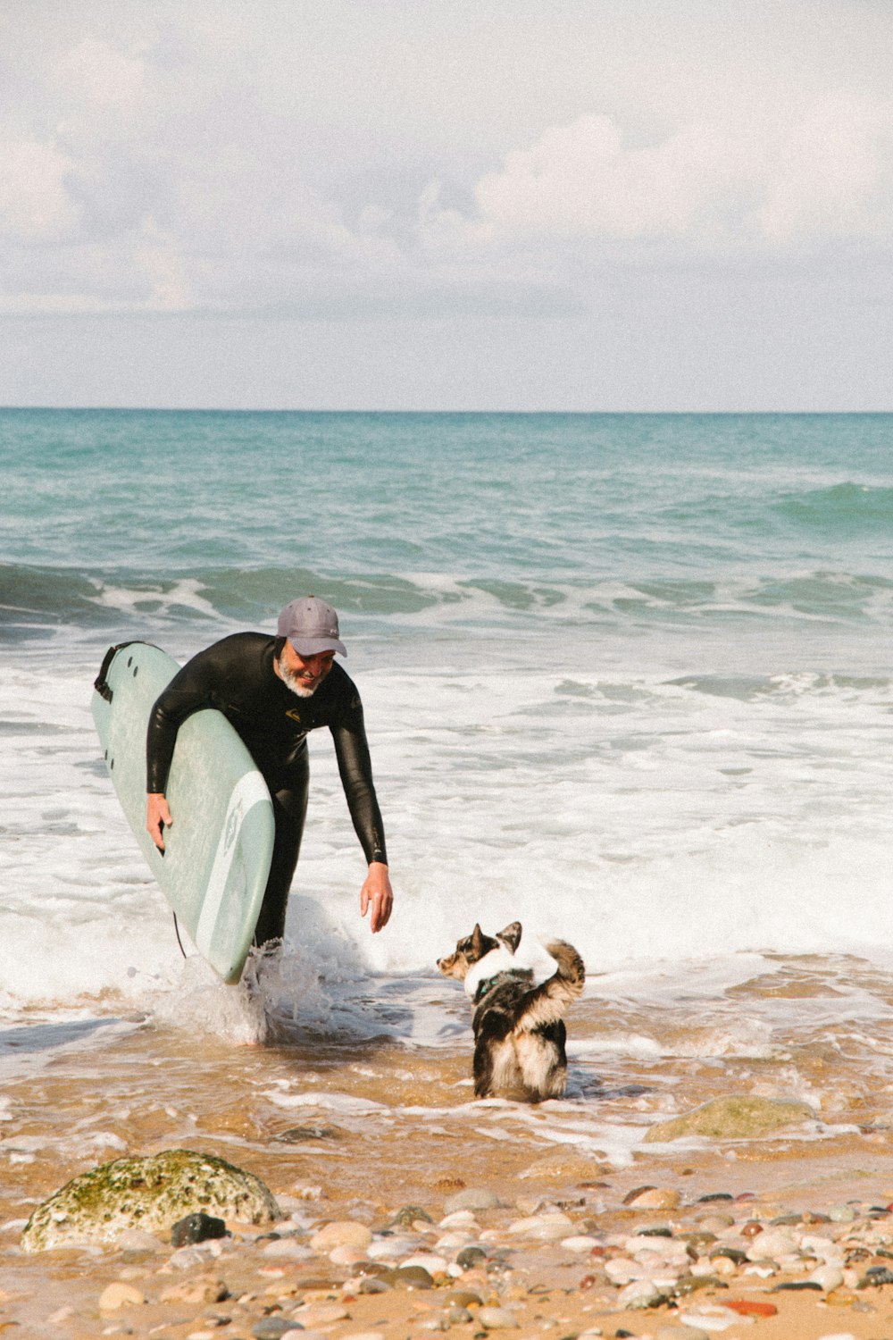 a man with a surfboard and two dogs in the water