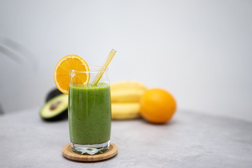 a green smoothie with an orange slice and a straw