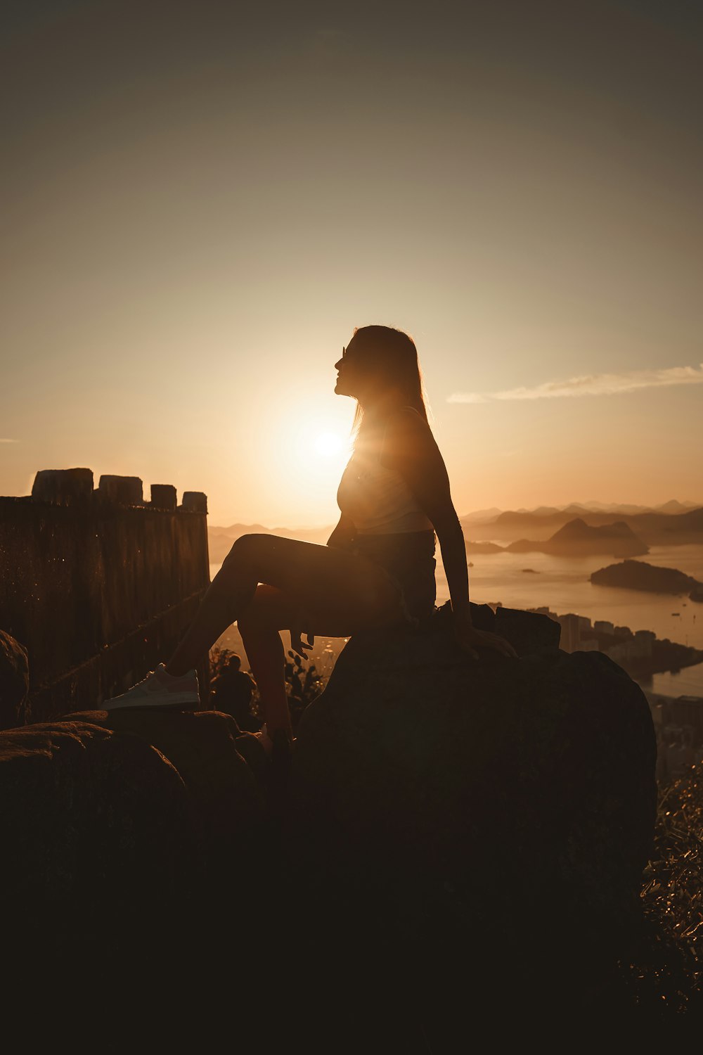 a woman sitting on top of a rock next to a body of water