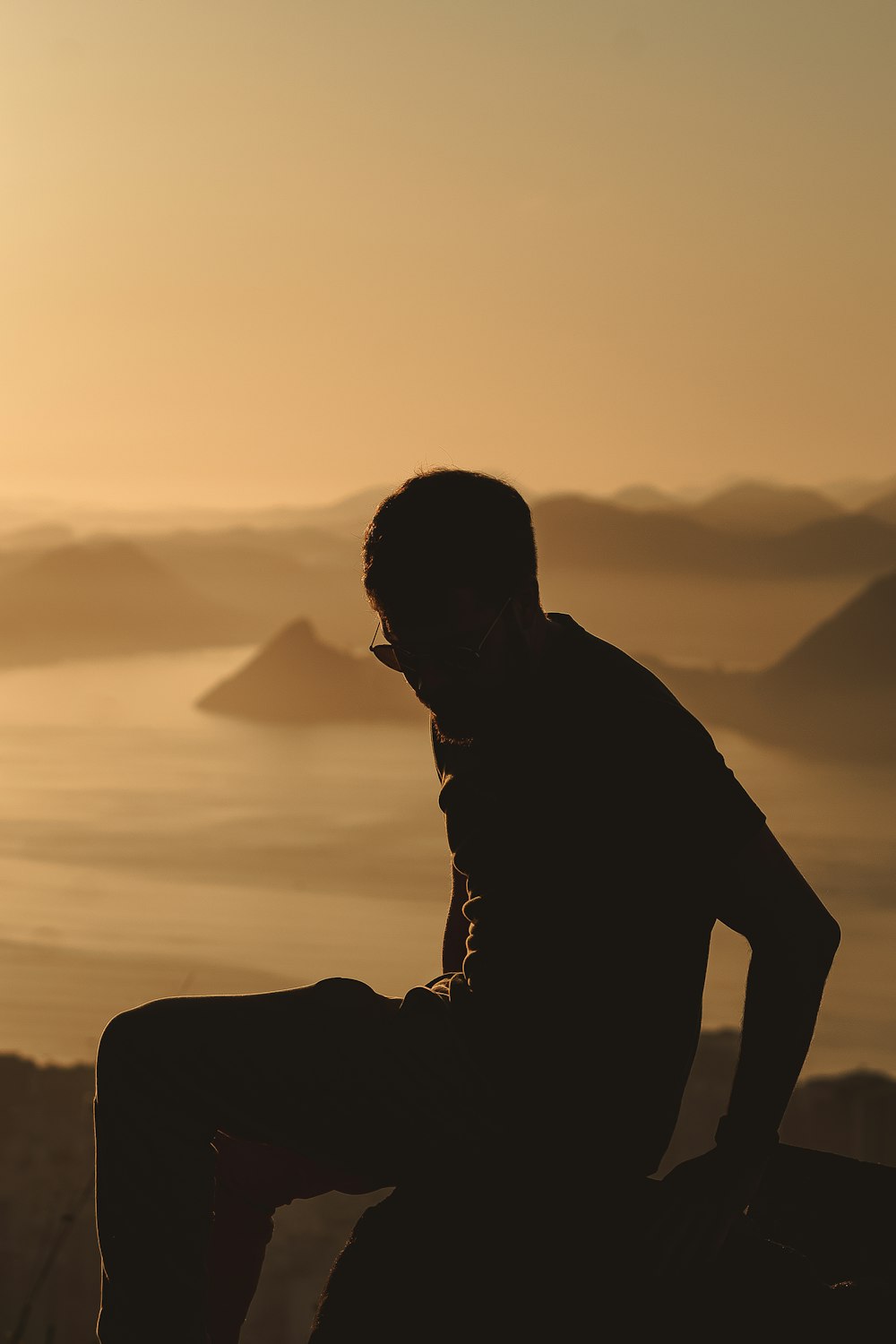 a man sitting on top of a mountain next to a body of water