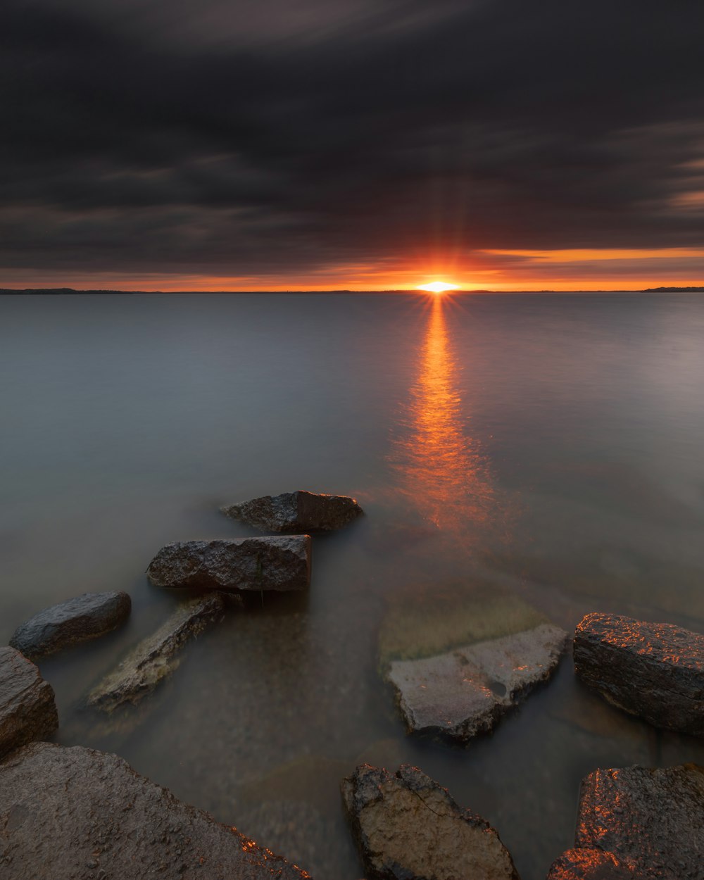 a sunset over a body of water with rocks in the foreground