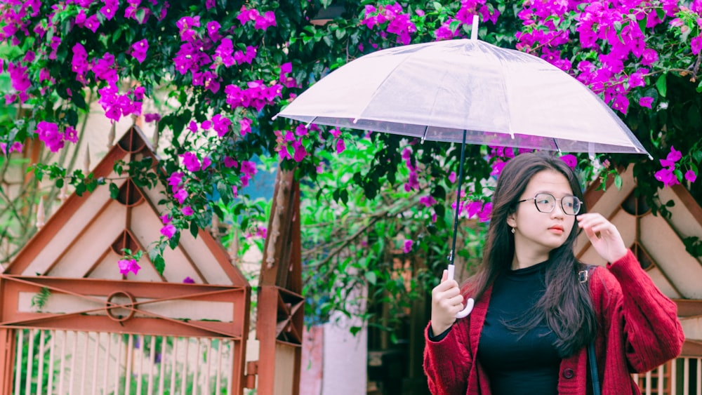 a woman holding a clear umbrella in front of purple flowers