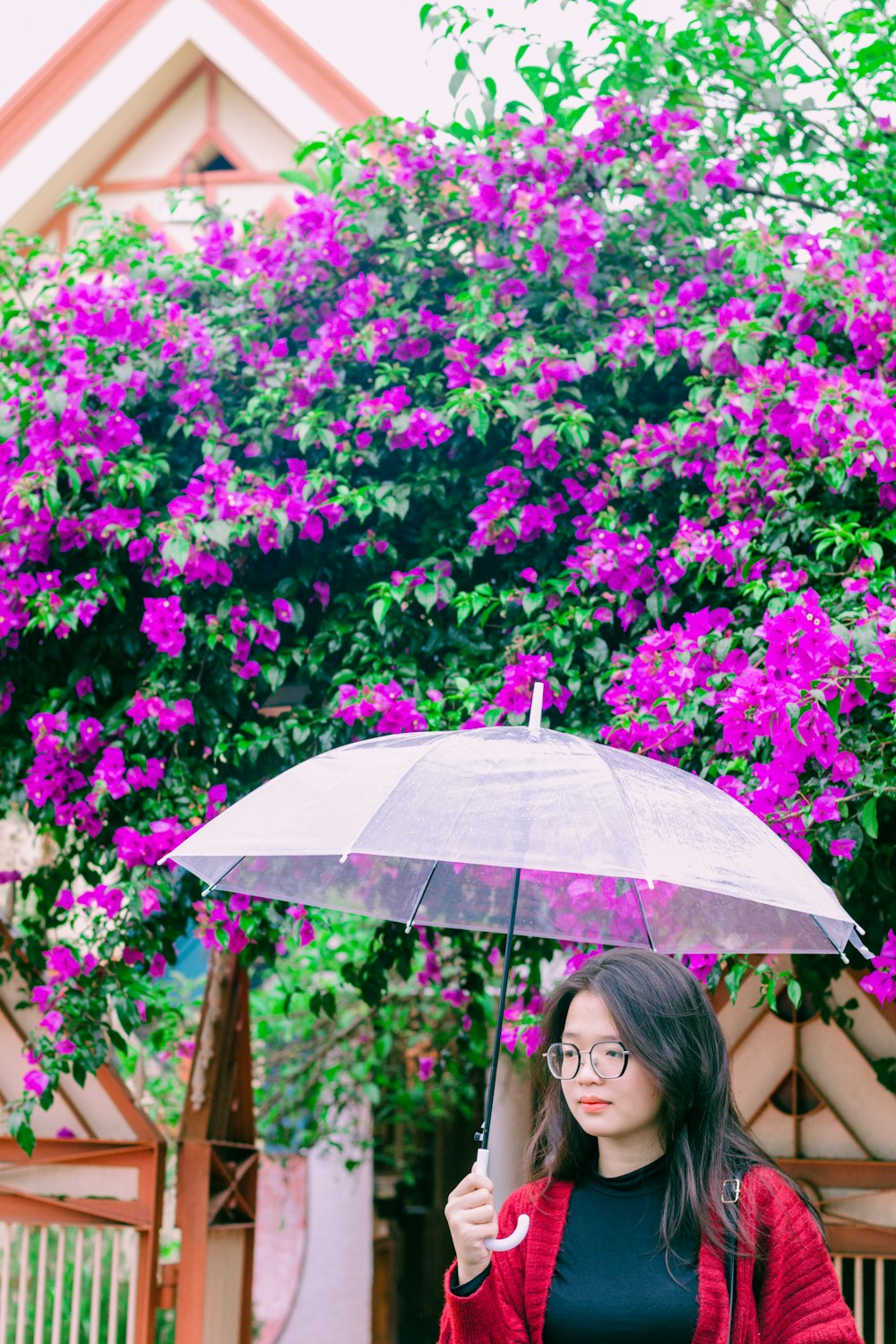 a woman holding an umbrella in front of a bush of purple flowers