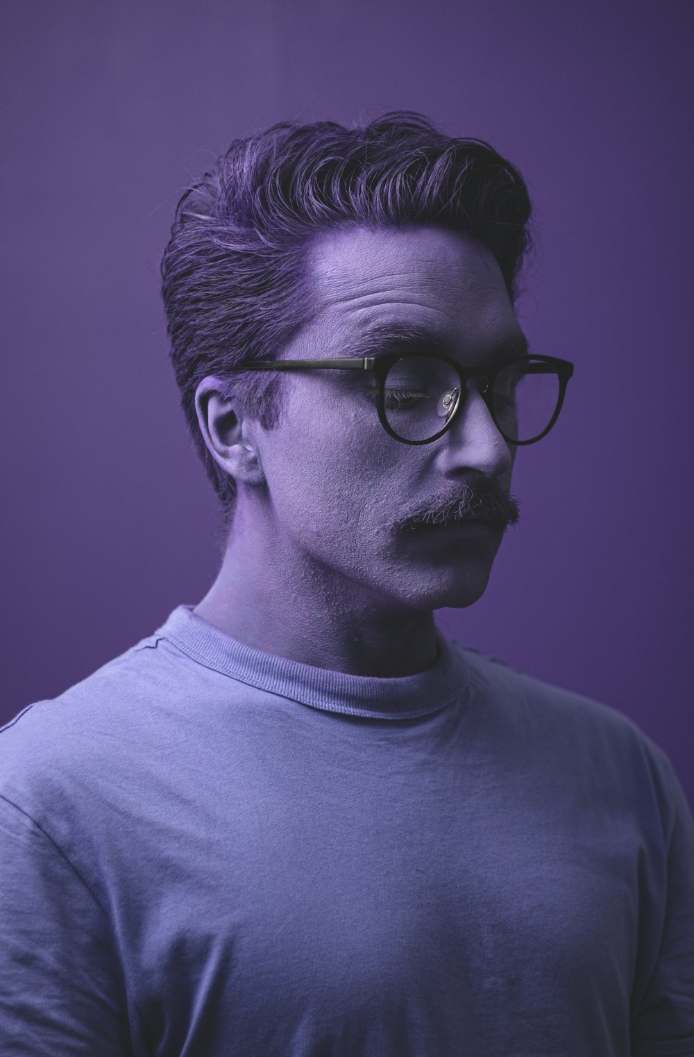 Un hombre con bigote y gafas sobre fondo púrpura