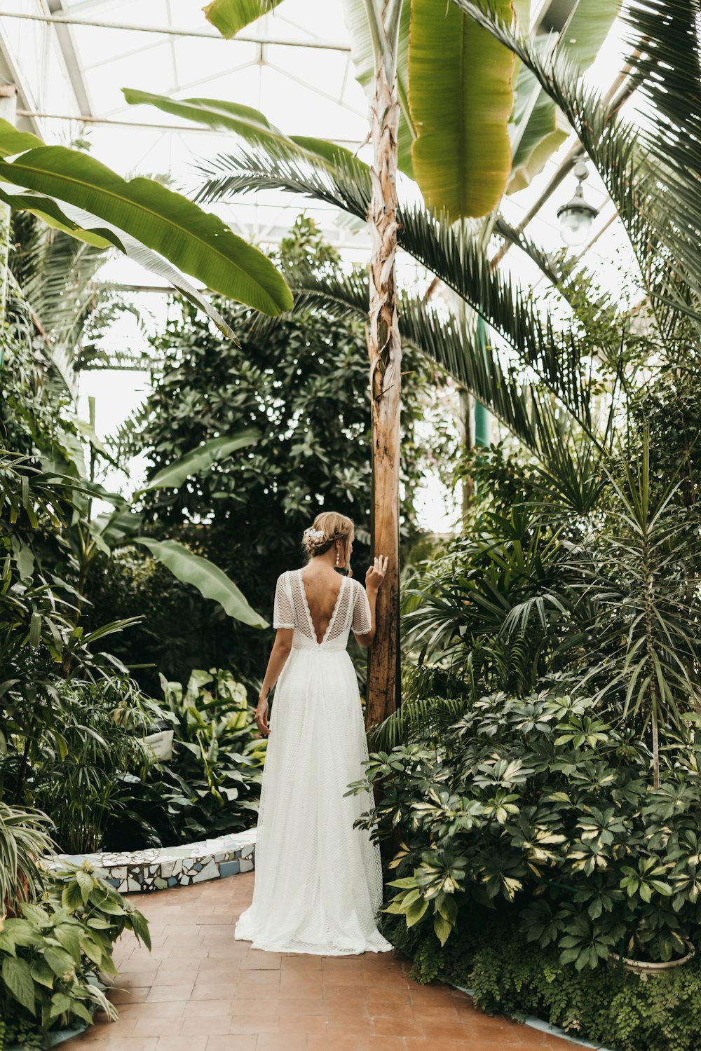 a woman in a white dress standing in a greenhouse