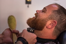 a bearded man getting his hair cut with a brush