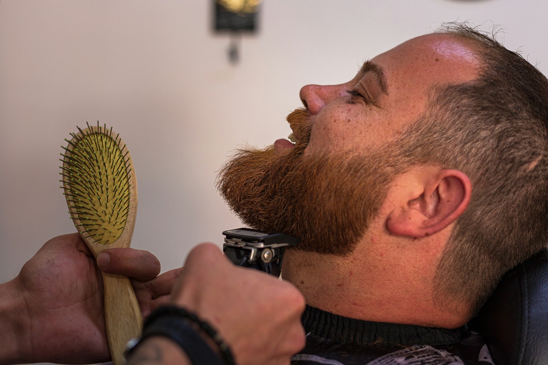 a bearded man getting his hair cut with a brush