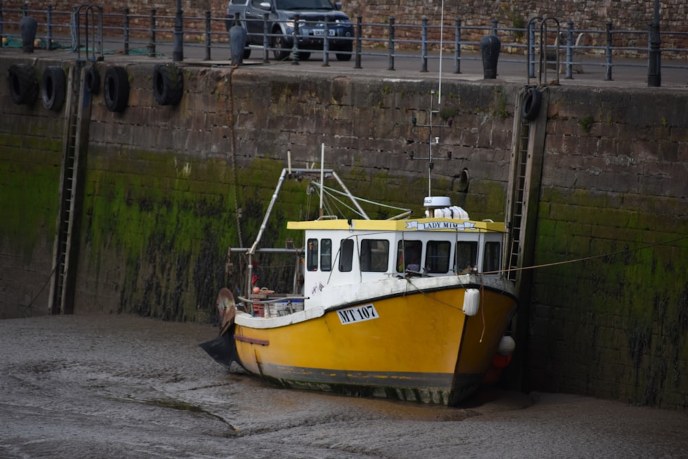 a yellow and white boat sitting next to a brick wall