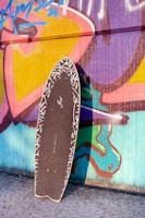 Photo of a sleek double kicktail skateboard parked against a colorful graffiti wall.