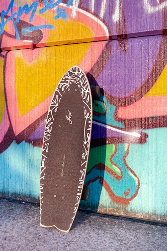 Close-up of a colorful skateboard deck with bold graphics leaning against a graffiti-covered wall.