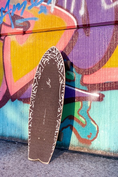 A vibrant skateboard deck leaning against a graffiti-covered wall in an urban skatepark.