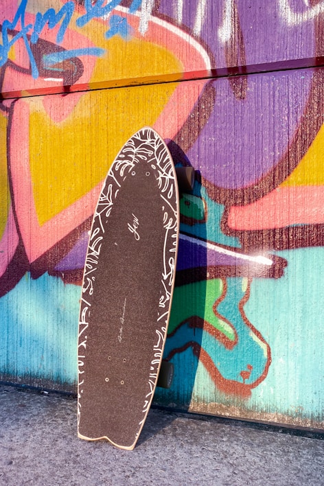 A sleek double kick skateboard resting against a graffiti-covered wall.