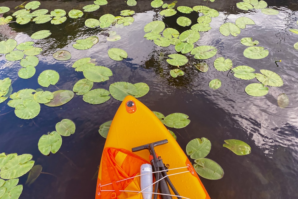 a yellow kayak floating on top of a lake filled with lily pads