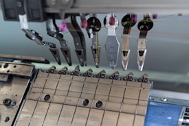 A close-up of a mechanical assembly featuring several metal components and tools, possibly part of a larger industrial or manufacturing machine. Various levers, grips, and fixtures are visible, suggesting a precise and technical function.