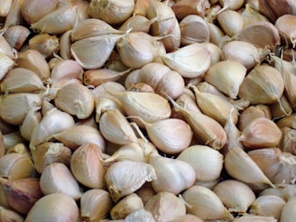 A large quantity of garlic bulbs piled together, each bulb consisting of several cloves with a papery, light brown husk.