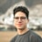 a young man wearing glasses standing in front of a mountain