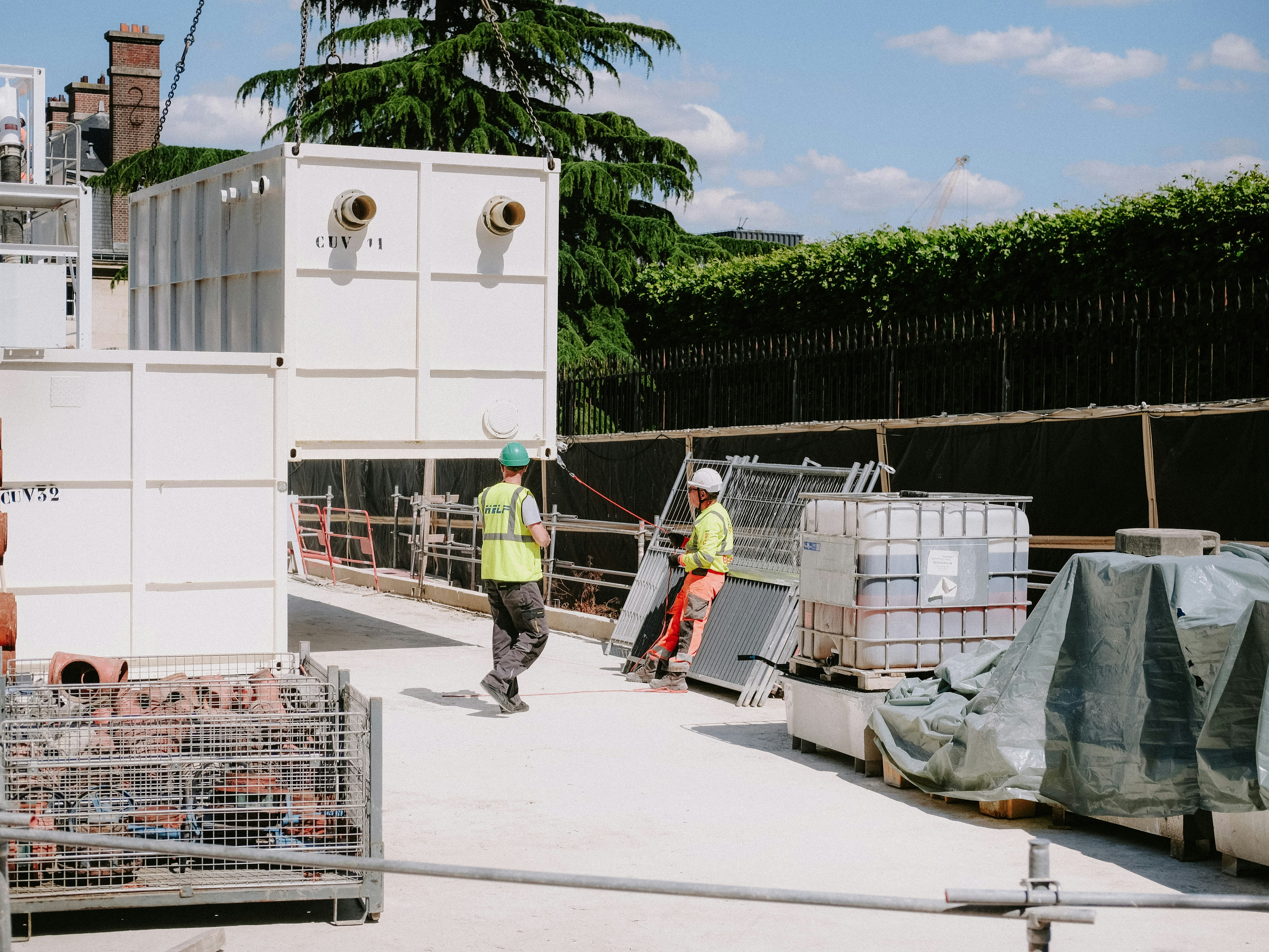 Construction workers in PPE on industrial site, bright daylight, steel structures, safety helmets, high-visibility vests