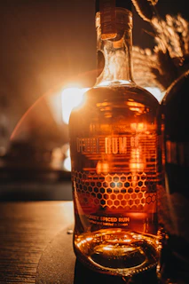 Close-up of a bottle of Madure Honey Rum Liqueur with honey dripping from a wooden honey dipper.