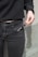 A person wearing a black sweater and dark jeans is holding a disposable vape pen with a visible label. The background appears to be a neutral-colored wall.