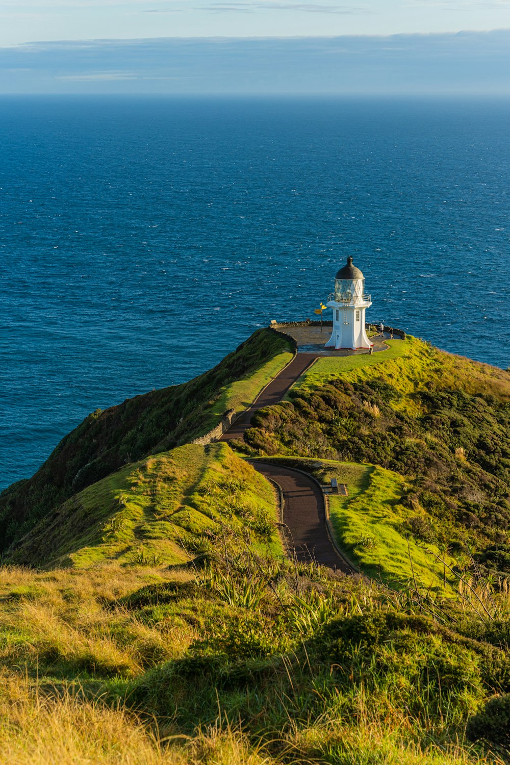 Ein Leuchtturm auf einem grasbewachsenen Hügel mit Blick auf den Ozean