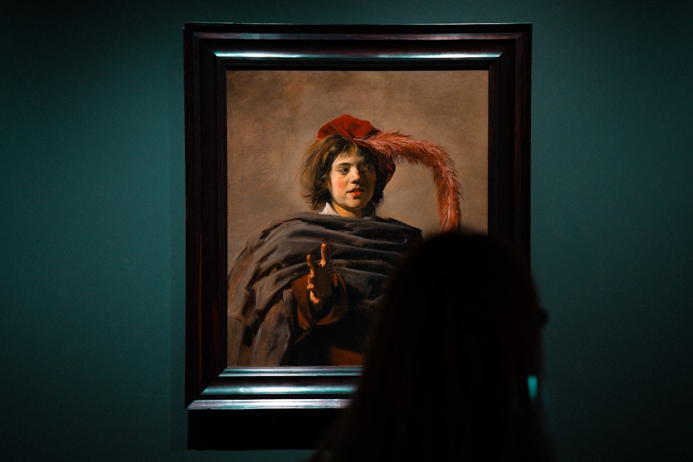 a woman looking at a painting of a woman with a red bow