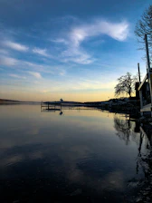 A peaceful lakeside view at sunset with a small dock and gentle waves.
