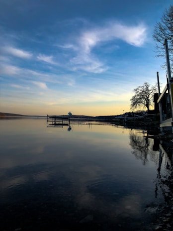 A serene lakeside view at sunset with warm orange and blue tones reflecting on the water.