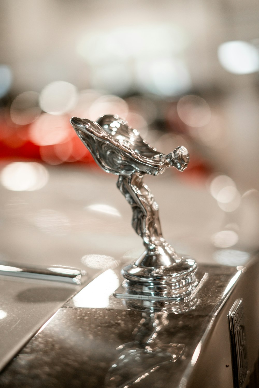 a silver car hood ornament with a red car in the background