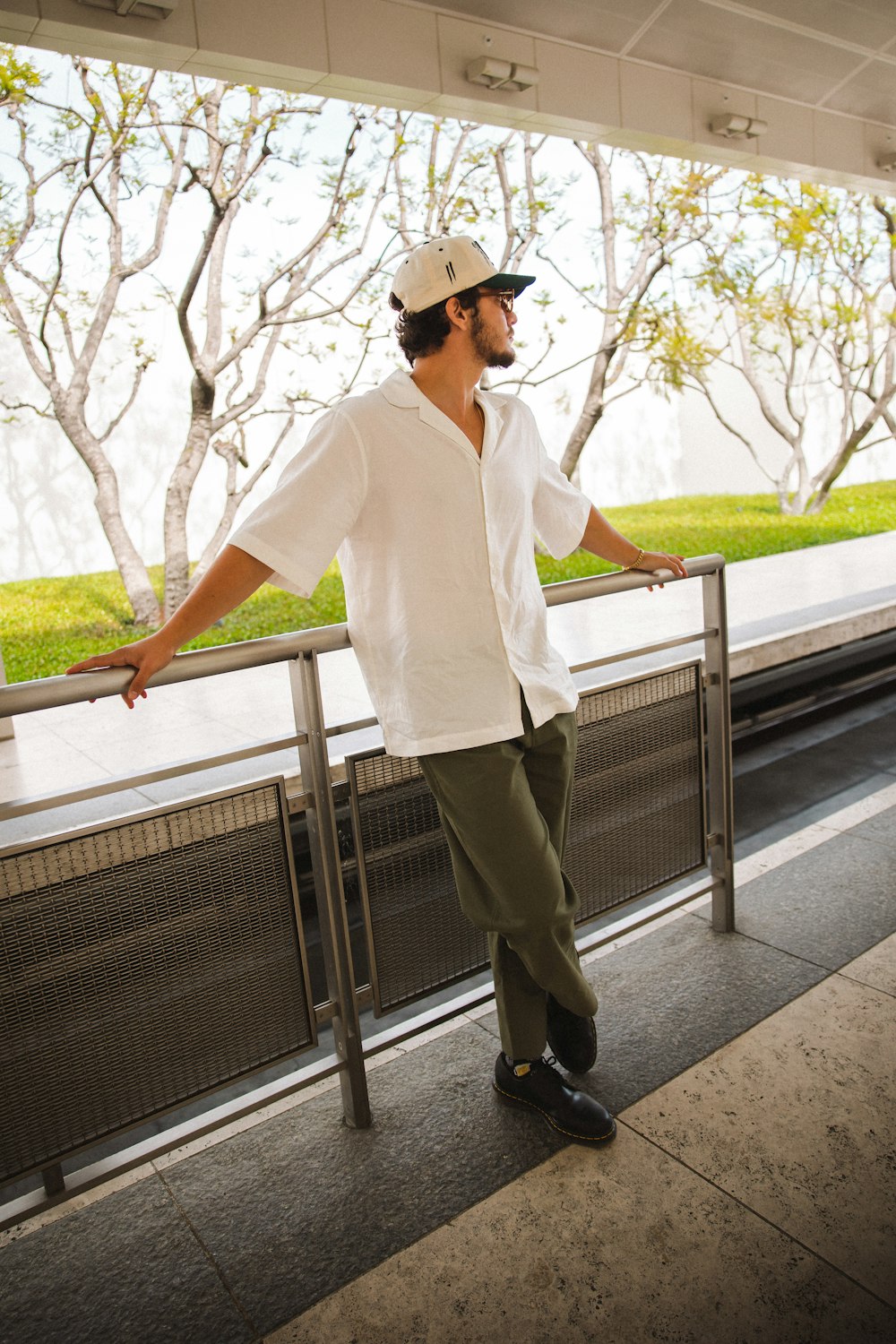 a man in a white shirt and hat leaning against a rail
