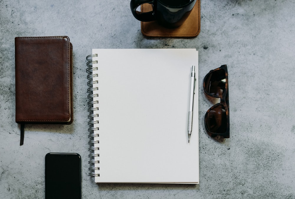 a notepad, pen, sunglasses, and a phone on a table