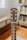 A close-up view of a guitar headstock, featuring tuning pegs and strings. The guitar is placed indoors with a blurred background showing wooden floors and a bookshelf.
