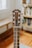 A close-up view of a guitar headstock, featuring tuning pegs and strings. The guitar is placed indoors with a blurred background showing wooden floors and a bookshelf.