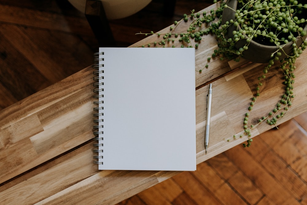 a notepad sitting on top of a wooden table next to a plant