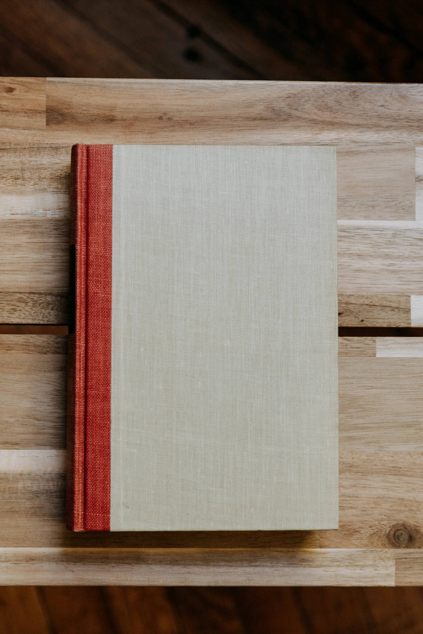 A linen-bound book with a red spine on a wooden table