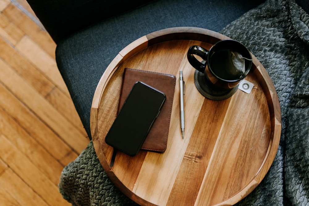 a wooden tray with a notebook, pen, and coffee cup on it