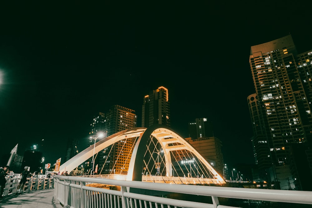 a bridge over a river at night with tall buildings in the background