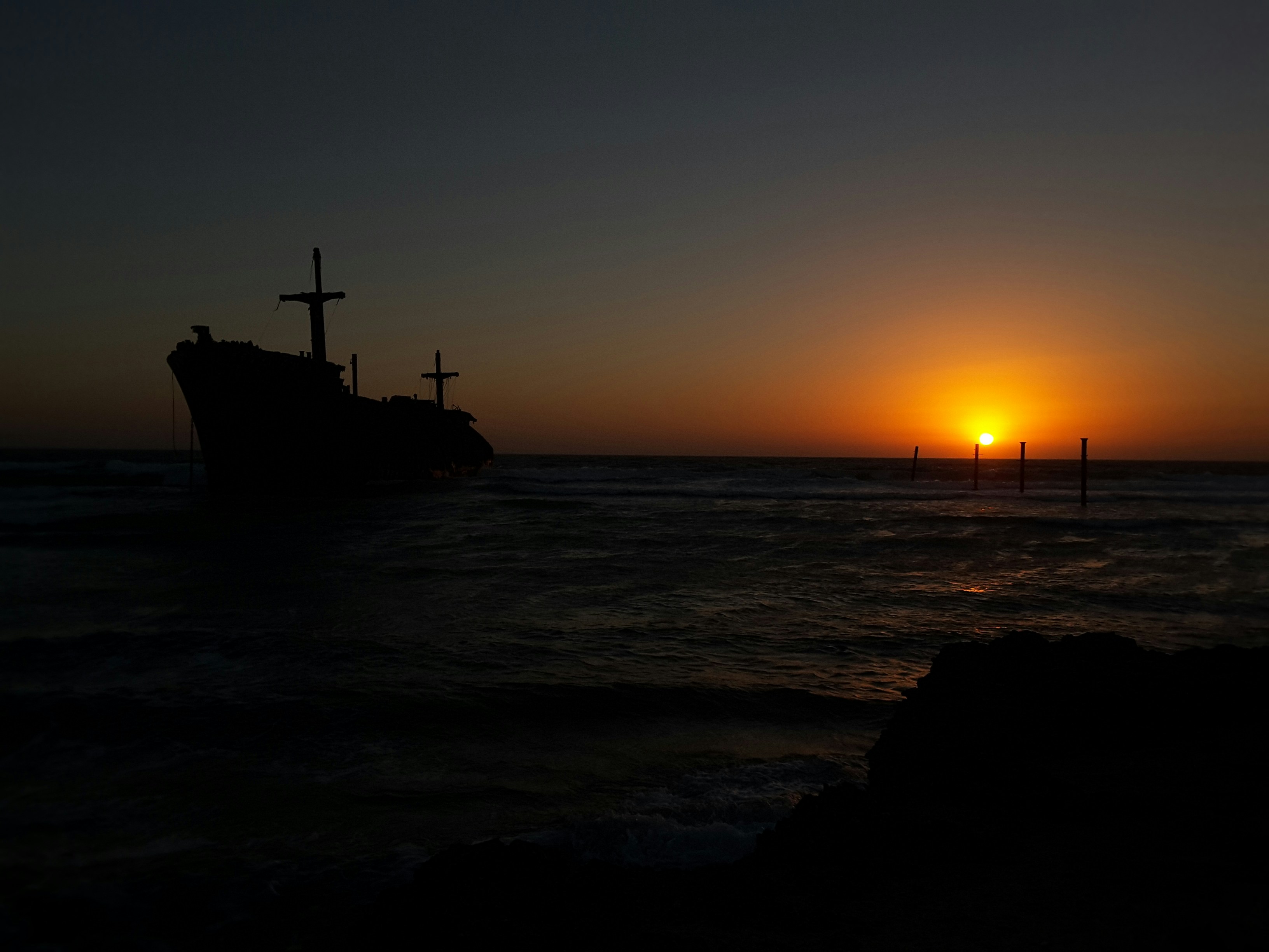 the sun is setting over the ocean with a boat in the water