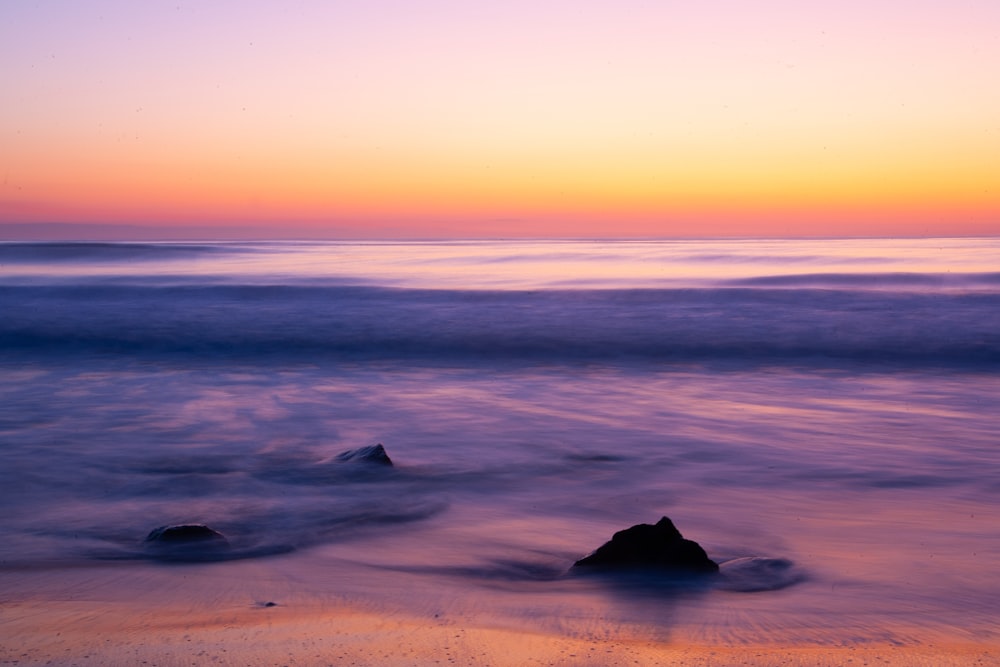 a sunset over the ocean with a rock in the foreground