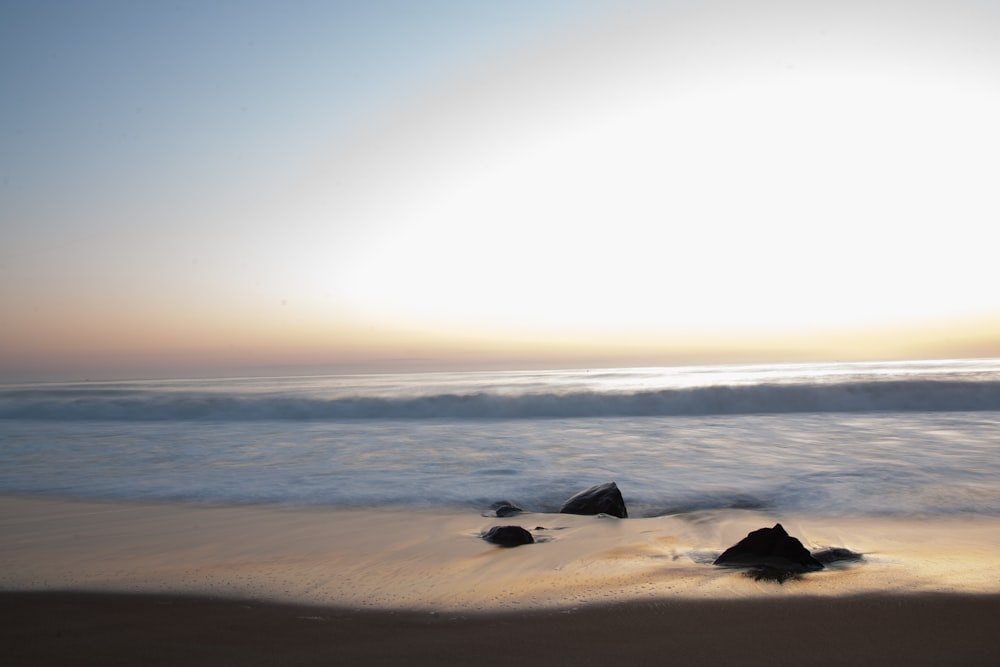 태양은 모래 위에 바위가있는 바다 위로지고 있습니다.