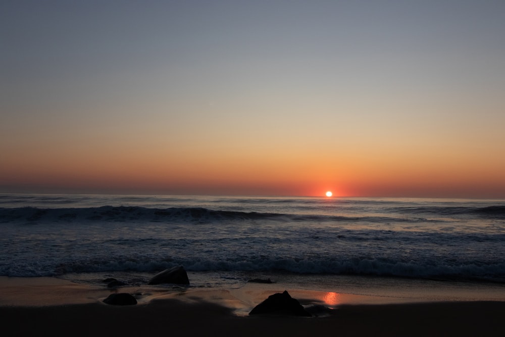 the sun is setting over the ocean on the beach