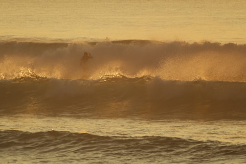 Surfer riding a powerful wave at sunset with vibrant colors.
