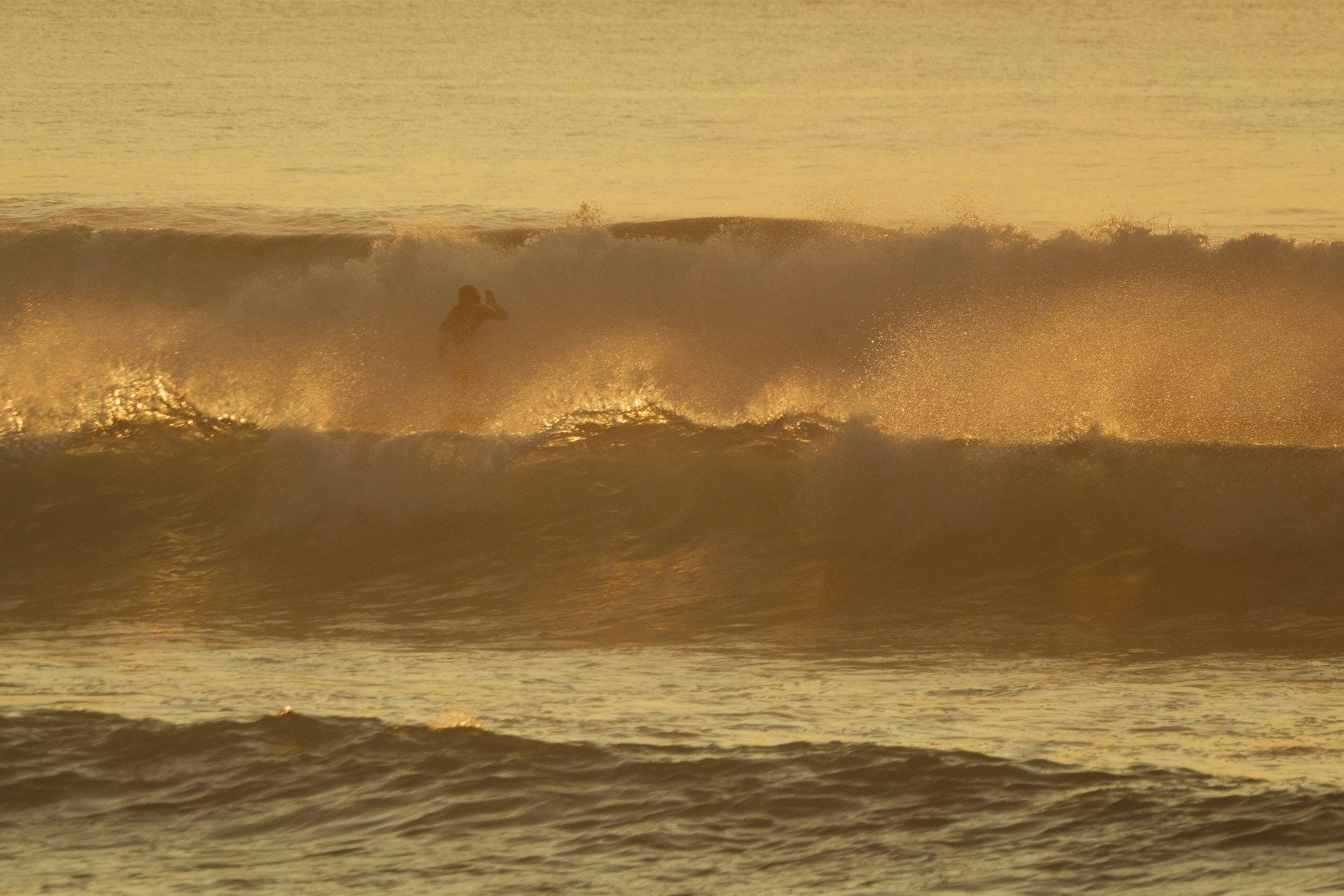 A surfer catching a powerful wave at sunset, with golden light reflecting on the water.