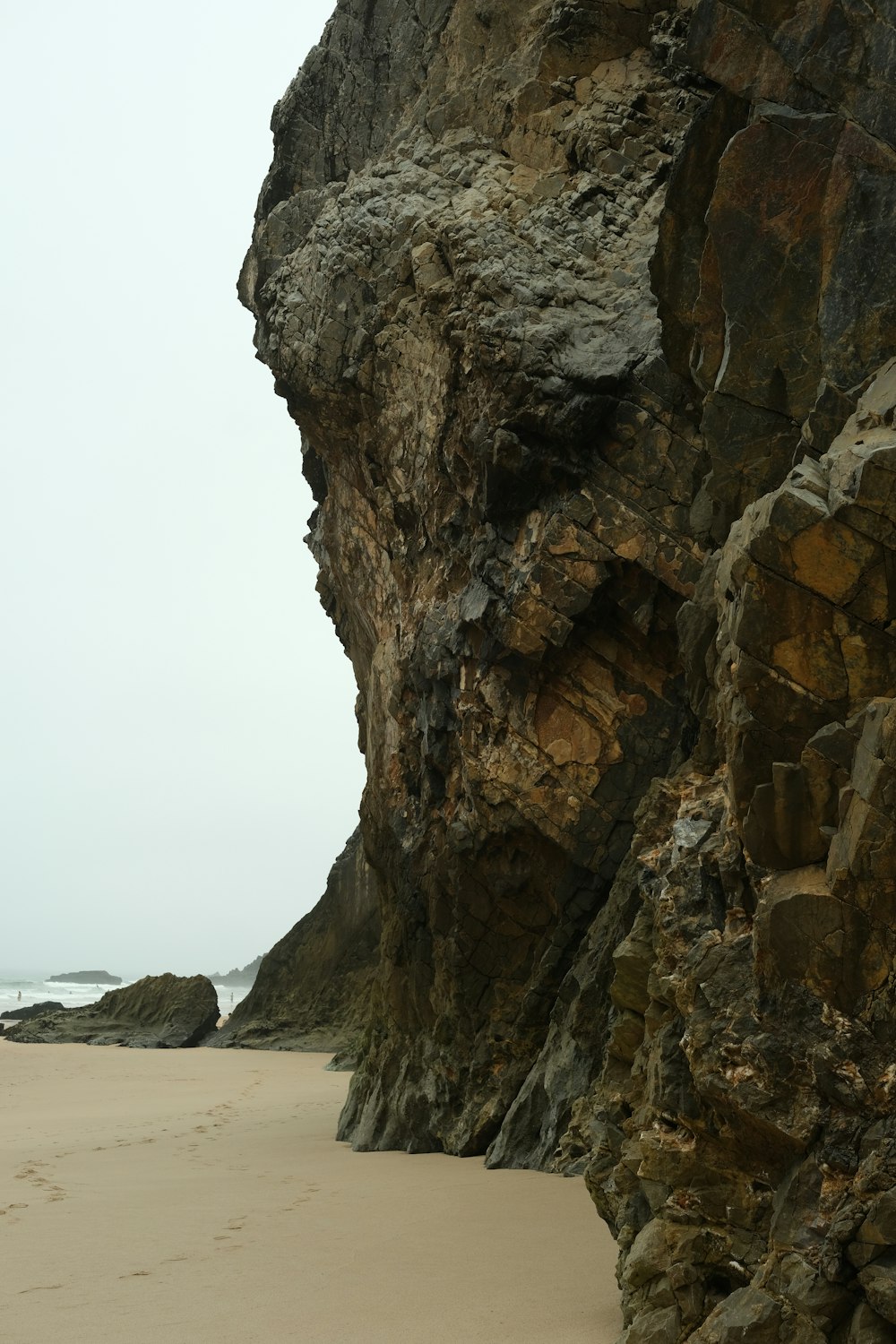 a person walking on a beach next to a large rock