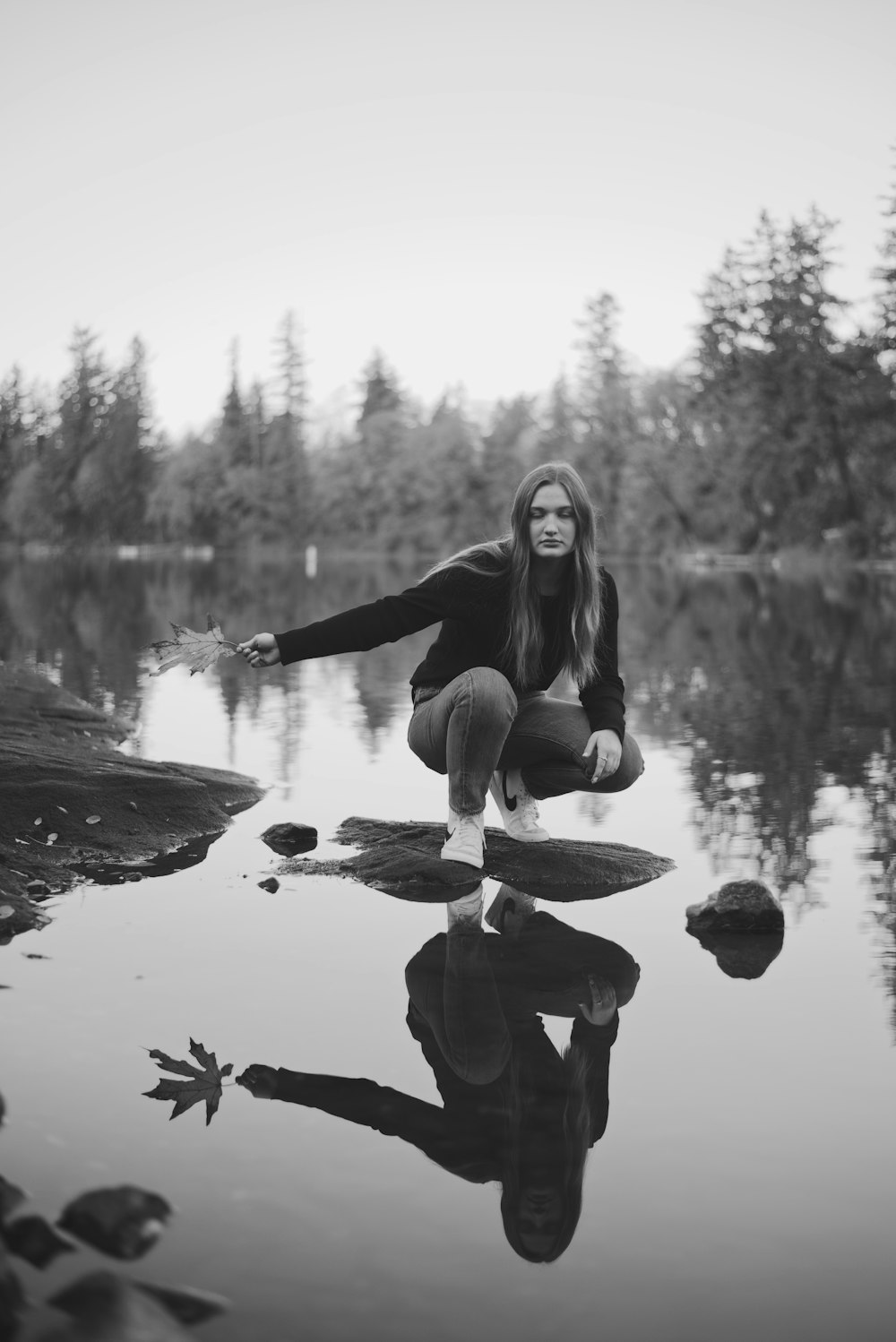 a woman kneeling on top of a rock next to a body of water