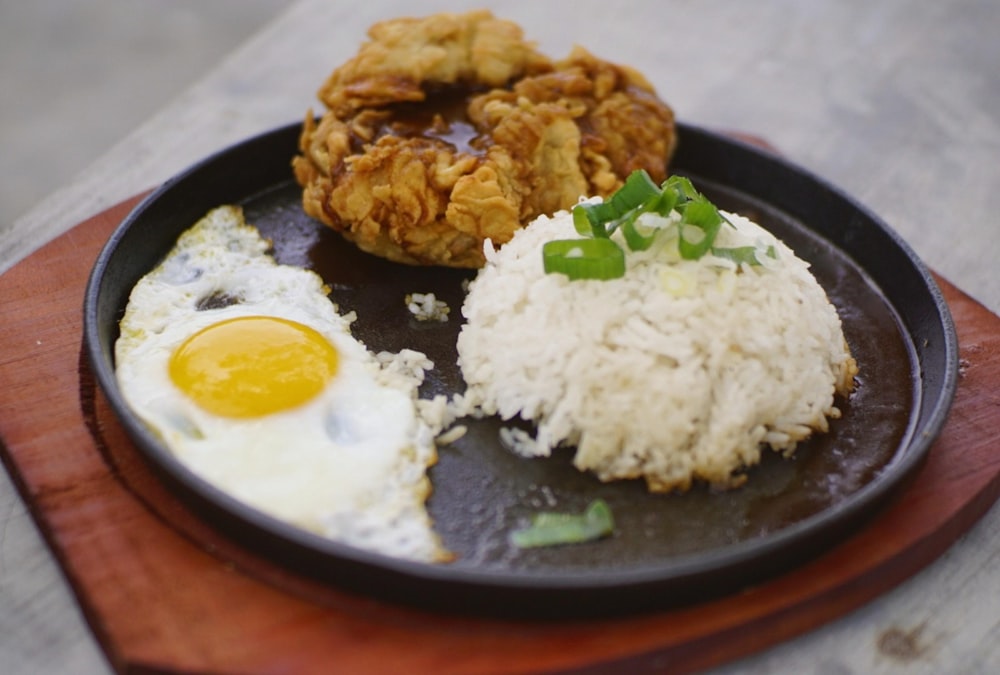 a plate of food with rice, fried egg and fried chicken