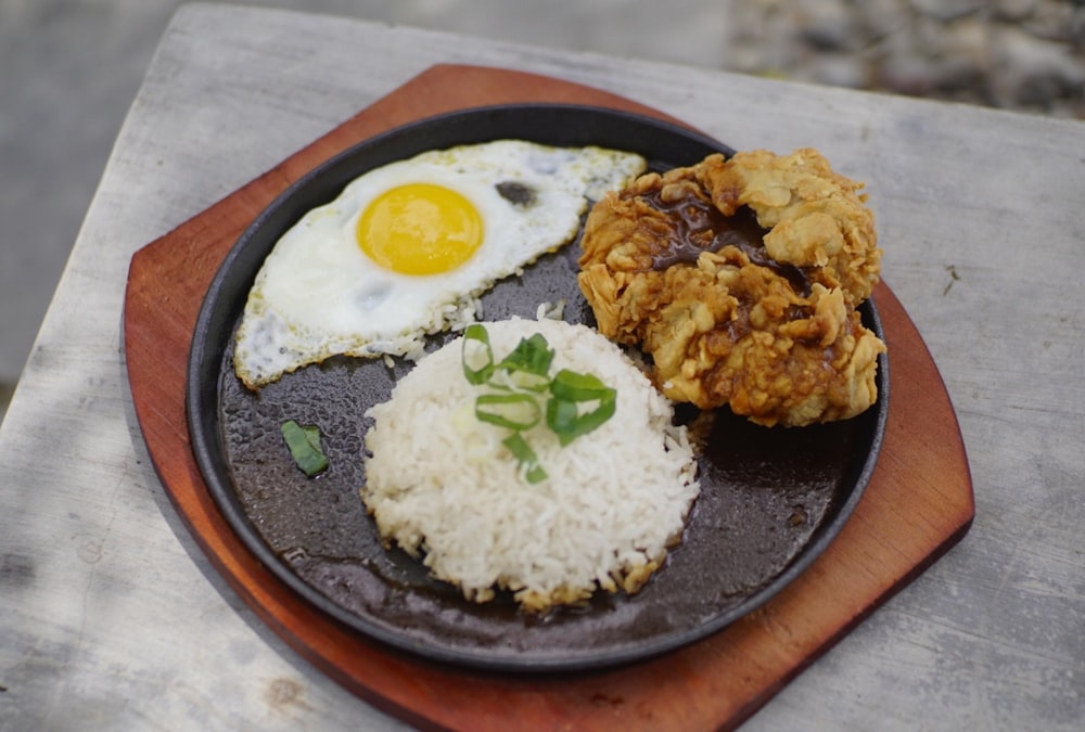 a plate of food with rice, fried eggs, and meat