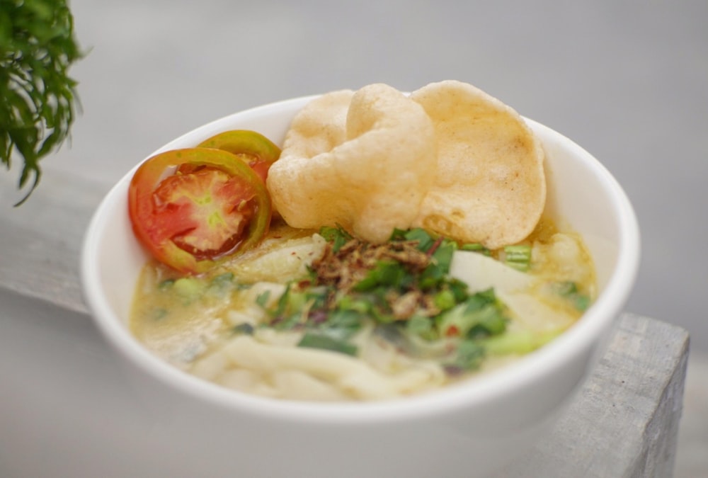 a bowl of soup with a tomato and chips