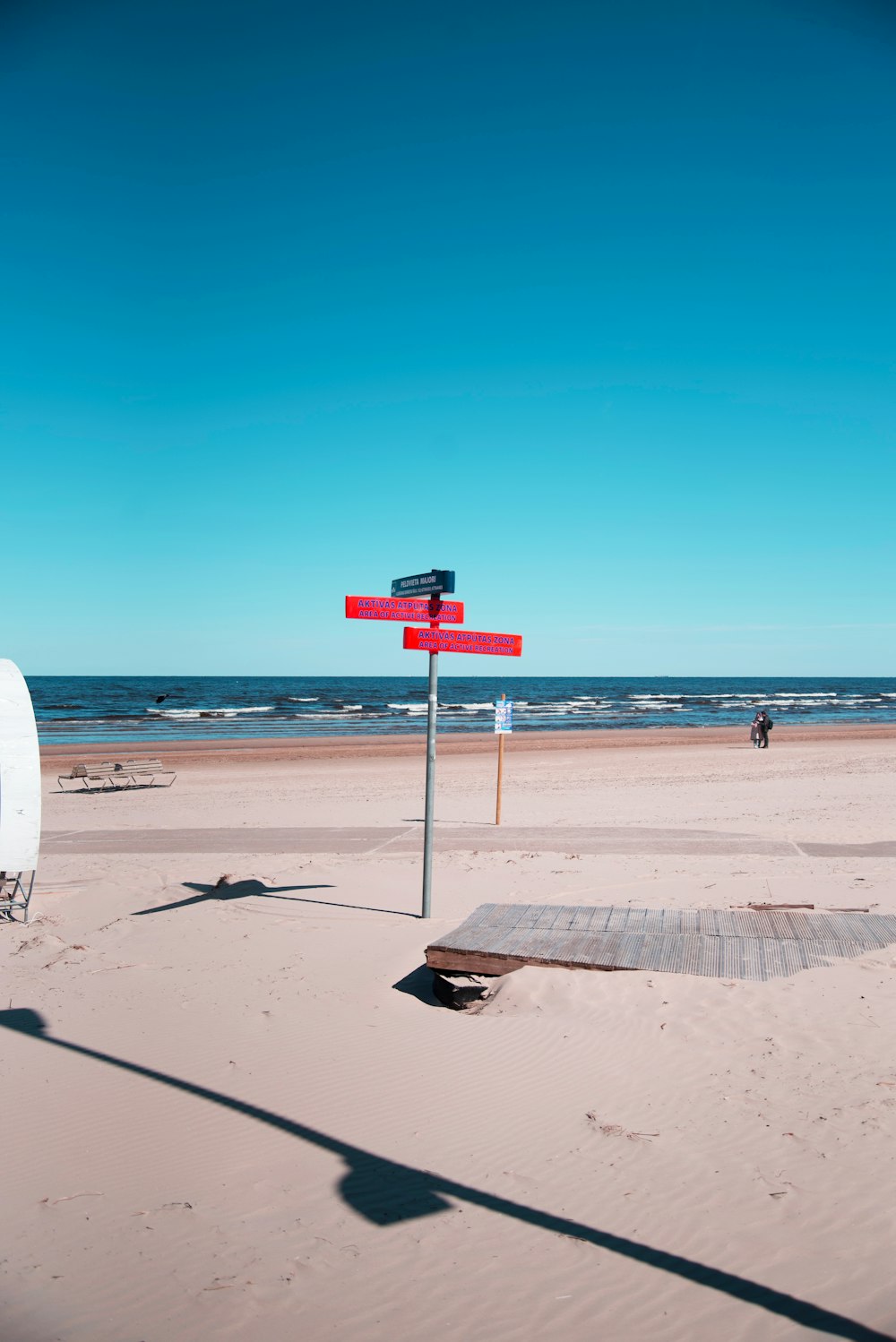 a red and white street sign sitting on top of a sandy beach