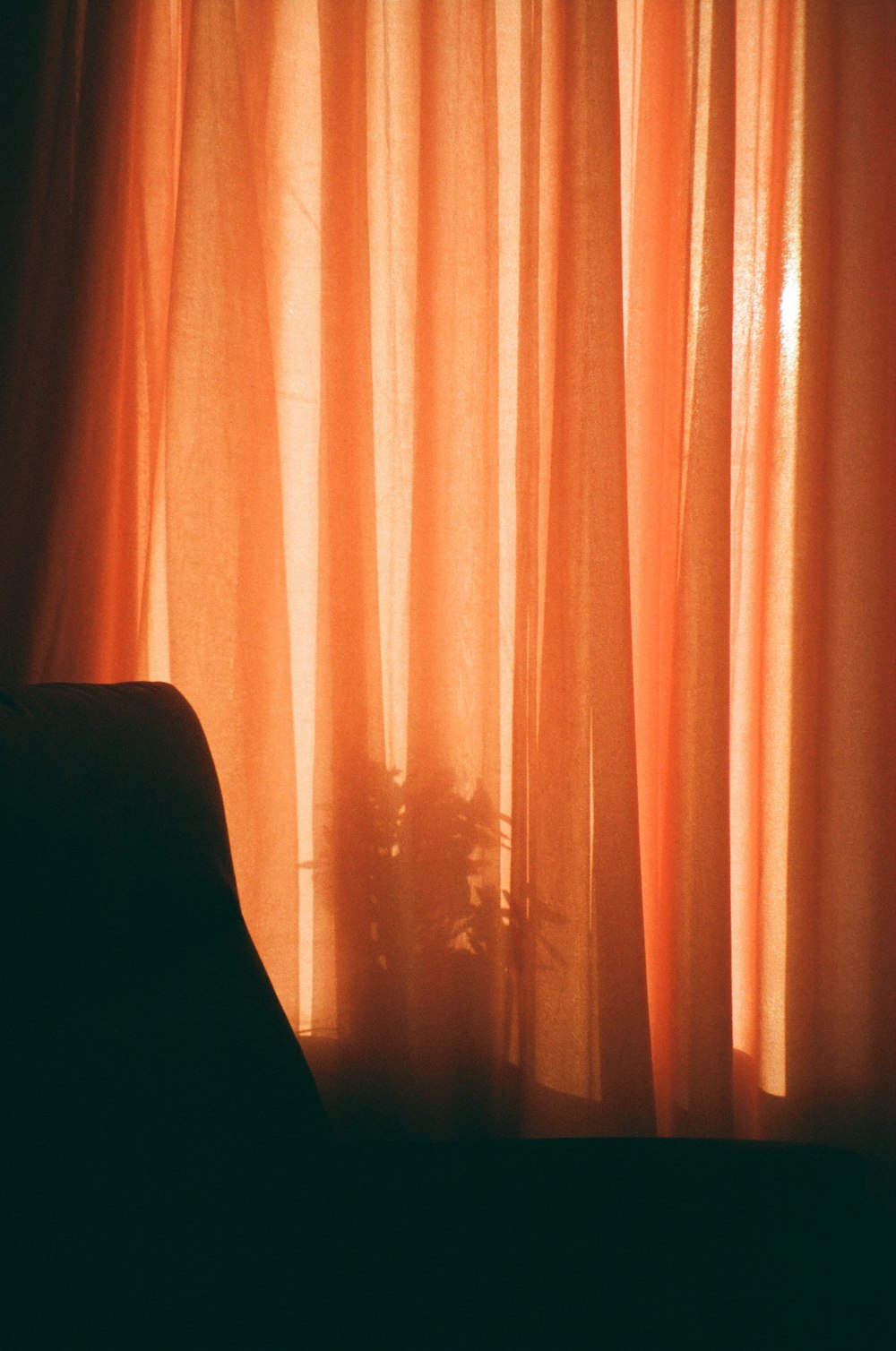a chair sitting in front of a window covered in orange curtains