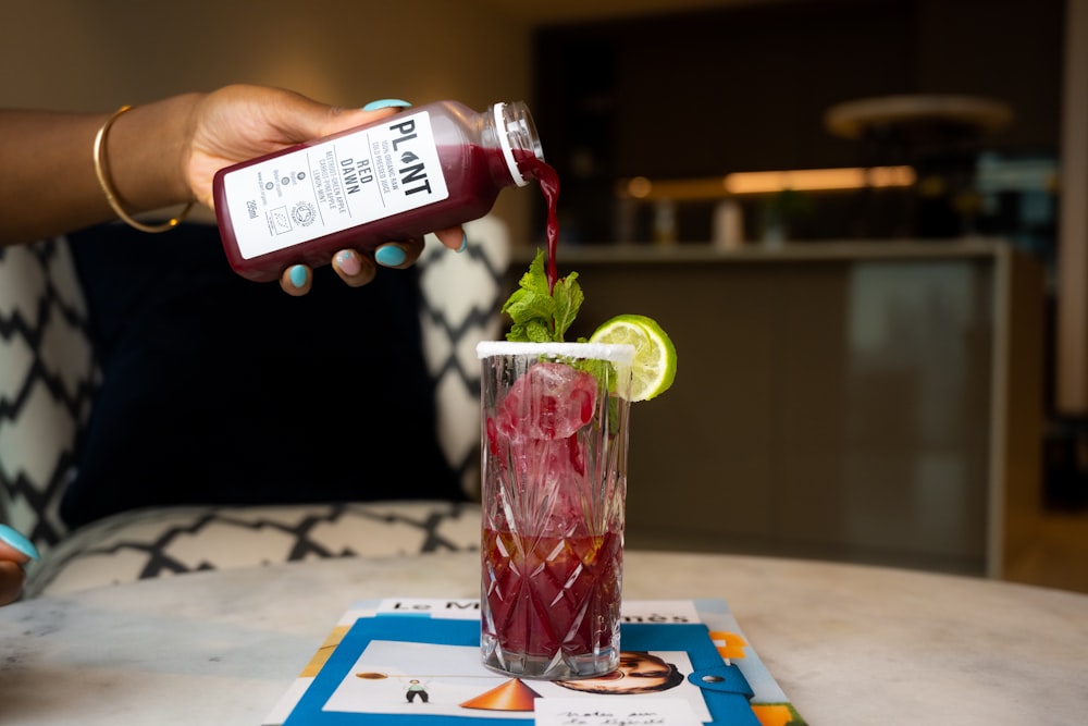 a person pouring a drink into a tall glass